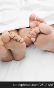 Close-up of a couple&acute;s feet with their child on the bed
