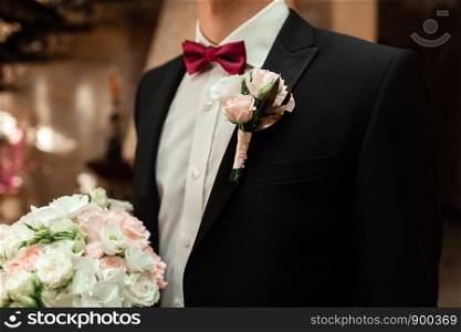Close-up of a cropped frame is a tender bouquet of roses in the hands of a groom. A men in a wedding suit with tie is holding flowers.. Close-up of a cropped frame is a tender bouquet of roses in the hands of a groom.