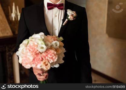 Close-up of a cropped frame is a tender bouquet of roses in the hands of a groom. A men in a wedding suit with tie is holding flowers. Close-up of a cropped frame is a tender bouquet of roses in the hands of a groom.