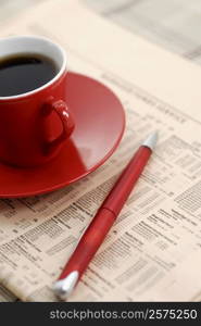 Close-up of a cup of black tea and pen on a newspaper