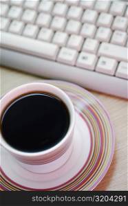 Close-up of a cup of black tea with a computer keyboard