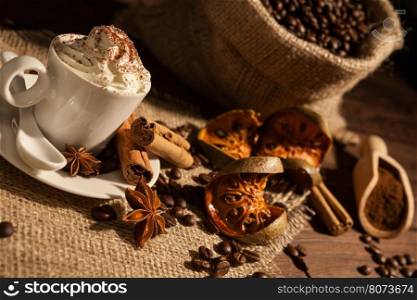 Close-up of a cup of coffee with whipped cream, cocoa powder, star anise, cinnamon and dried orange fruit