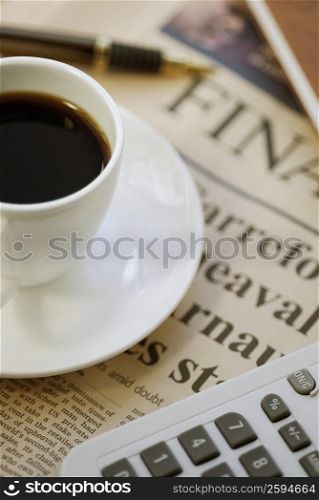 Close-up of a cup of tea with a calculator on a financial newspaper