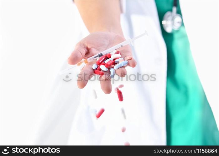 Close-up of a doctor hand holding a syringe with a needle and dropping several medicine pills and capsules on an out of focus background. Healthcare concept.. doctor hand dropping assorted pills and capsules
