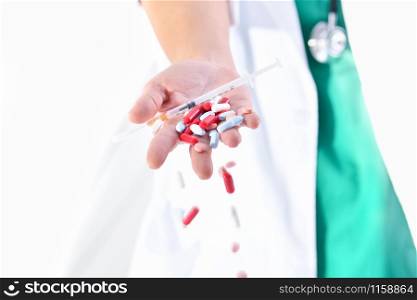 Close-up of a doctor hand holding a syringe with a needle and dropping several medicine pills and capsules on an out of focus background. Healthcare concept.. doctor hand dropping assorted pills and capsules