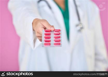 Close-up of a doctor hand showing a blister of red medicine capsules to the camera on an out of focus background. Healthcare concept.. Blister with red capsules held by a doctor
