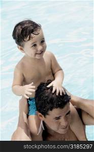 Close-up of a father carrying his son on his shoulders in a swimming pool