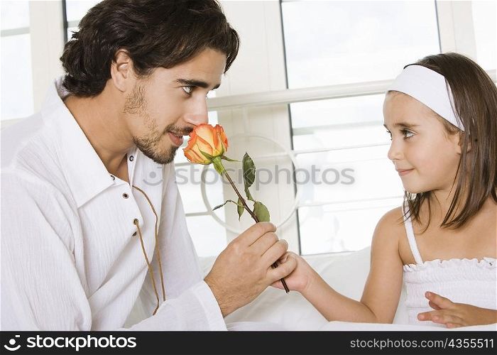 Close-up of a father sitting with his daughter smelling a rose