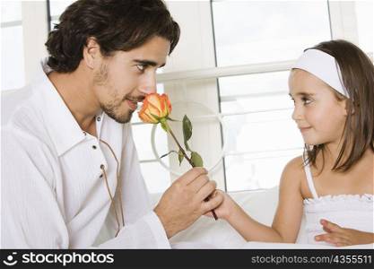 Close-up of a father sitting with his daughter smelling a rose