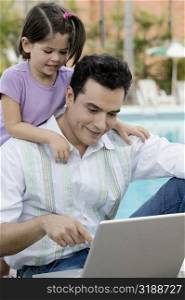Close-up of a father using a laptop with his daughter standing behind him