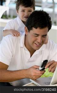 Close-up of a father using a mobile phone with his son standing behind him