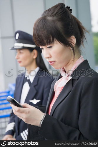 Close-up of a female cabin crew holding a mobile phone with a female pilot standing in the background