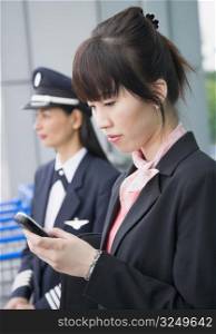 Close-up of a female cabin crew holding a mobile phone with a female pilot standing in the background