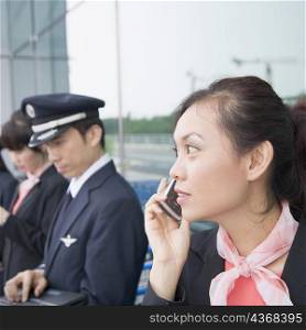 Close-up of a female cabin crew talking on a mobile phone with a pilot using a laptop in the background