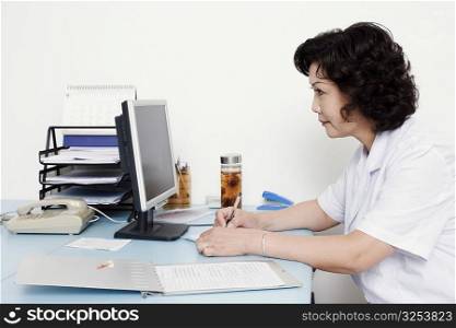 Close-up of a female doctor looking at a computer monitor and writing on a notepad