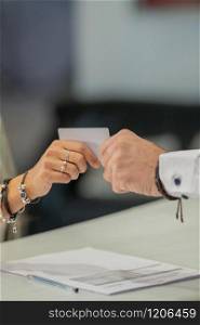 Close-up of a female hand giving a credit card to a male hand over a counter with papers on an out of focus background. Commerce concept.. Woman giving credit card to man at a counter