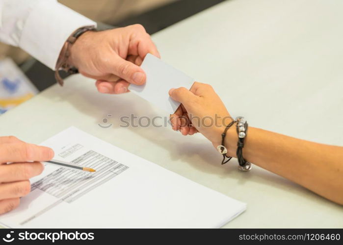 Close-up of a female hand giving a credit card to a male hand next to a bill over a table on an out of focus background. Commerce concept.. Woman giving credit card to man over a bill