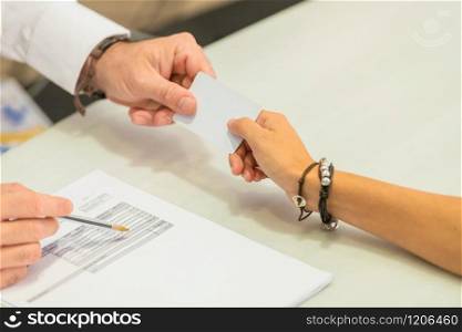 Close-up of a female hand giving a credit card to a male hand next to a bill over a table on an out of focus background. Commerce concept.. Woman giving credit card to man over a bill