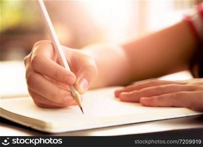 Close up of a female hand using a pencil writing ,drawing on a white book.Close up of casual woman writing on paper notebook or old diary on desk at home
