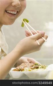 Close-up of a female office worker having lunch with chopsticks and smiling