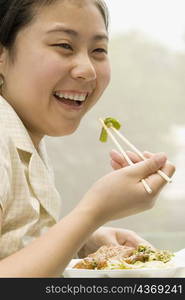 Close-up of a female office worker having lunch with chopsticks and smiling