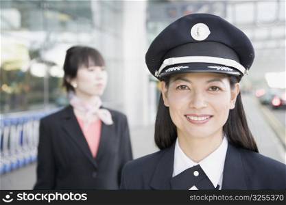 Close-up of a female pilot smiling with a female cabin crew behind her