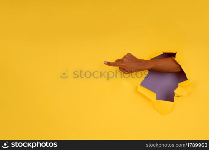 Close-up of a finger pointing something through a hole in a paper wall. Advertising and promotion concept.