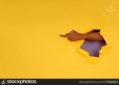 Close-up of a finger pointing something through a hole in a paper wall. Advertising and promotion concept.