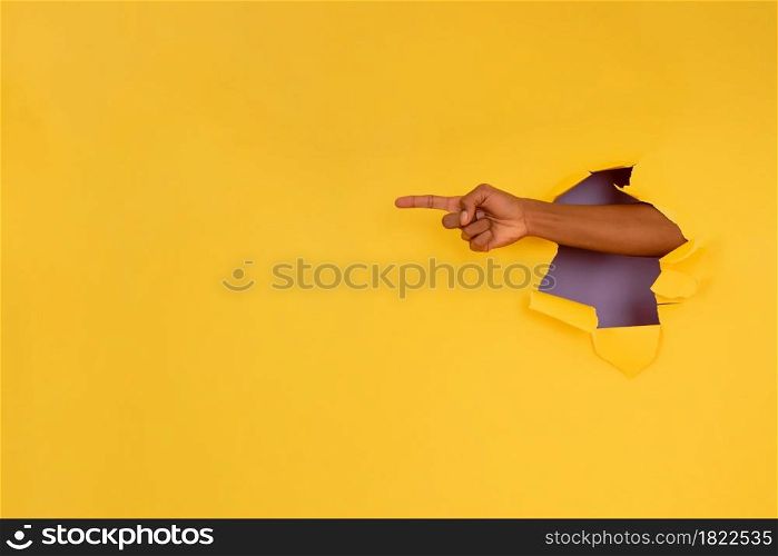 Close-up of a finger pointing something through a hole in a paper wall. Advertising and promotion concept.