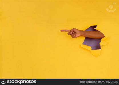 Close-up of a finger pointing something through a hole in a paper wall. Advertising and promotion concept.
