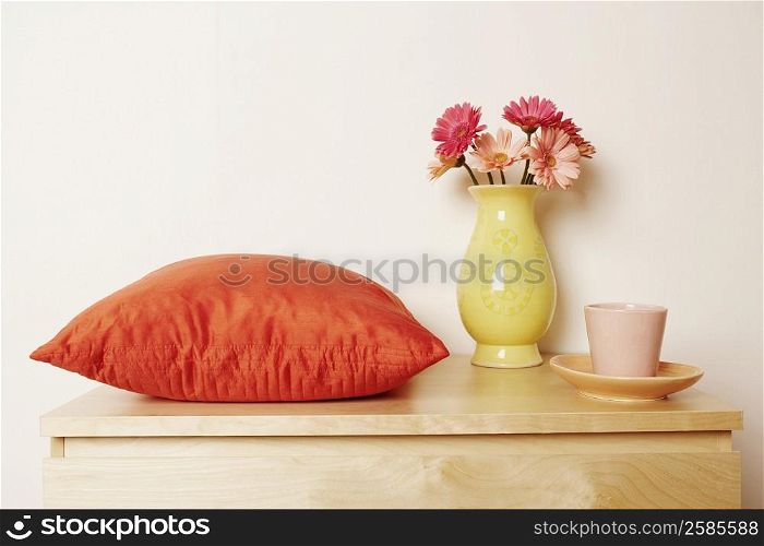 Close-up of a flower vase and a cushion with a cup on the table