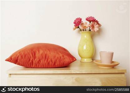Close-up of a flower vase and a cushion with a cup on the table