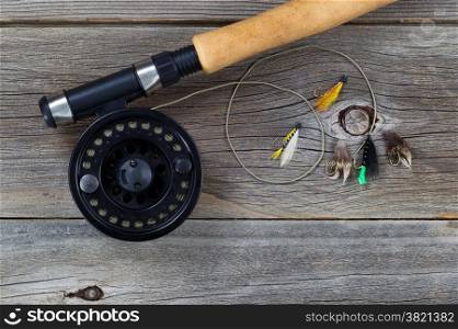 Close up of a fly reel, with line and assorted flies, and partial cork handled pole on rustic wooden boards