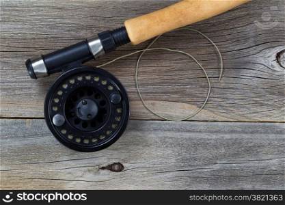 Close up of a fly reel, with line, and partial cork handled pole on rustic wood