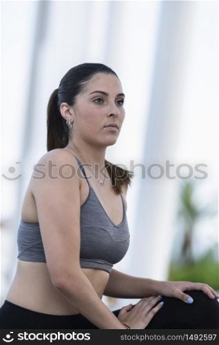 Close up of a focused young woman wearing sports bra and tights stretching outdoors on an out of focus background. Healthy lifestyle concept.