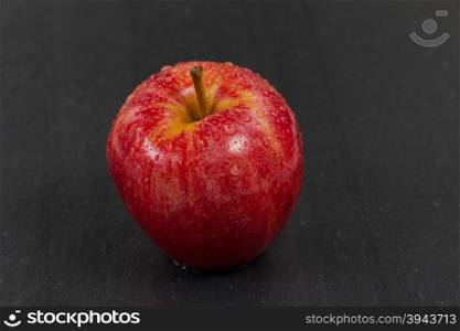 Close up of a fresh whole red apple, covered with water droplets, with natural slate stone underneath. Selective focus on front part of fruit.