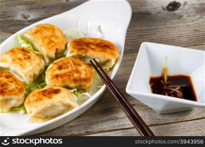 Close up of a front view of Chinese dumpling with sauce in bowl with chopsticks on rustic wood. Selective focus on tip of chopsticks.