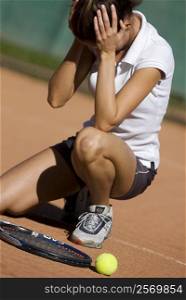 Close-up of a frustrated young woman crouching in a tennis court