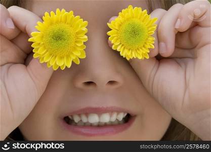 Close-up of a girl covering her eyes with flowers