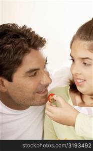Close-up of a girl feeding her father a strawberry