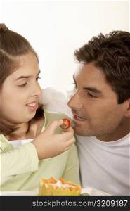 Close-up of a girl feeding her father a strawberry