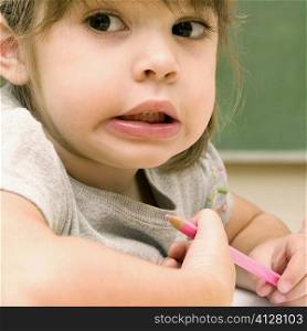Close-up of a girl holding a colored pencil and making a face