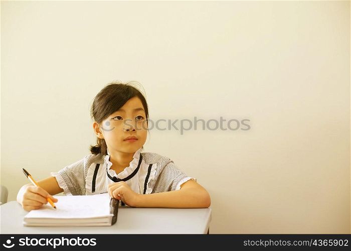 Close-up of a girl holding a pen on a spiral notebook in the classroom