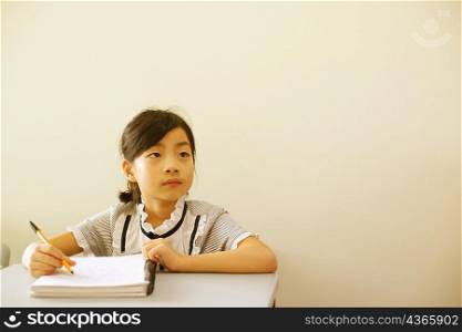 Close-up of a girl holding a pen on a spiral notebook in the classroom