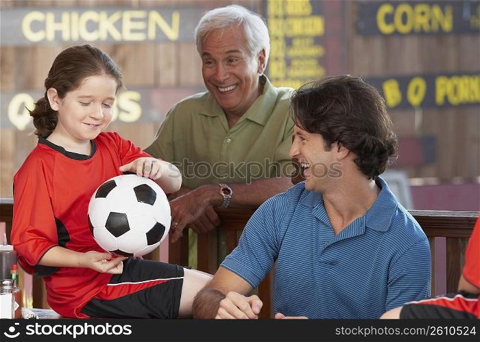 Close-up of a girl holding a soccer ball with her father and grandfather looking at her