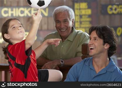 Close-up of a girl playing with a soccer ball with her father and grandfather beside her