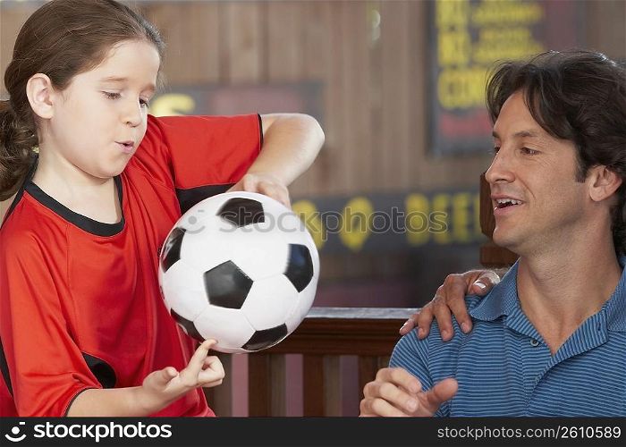 Close-up of a girl playing with a soccer ball with her father looking at her