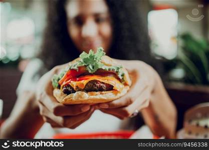 Close-up of a girl showing appetizing hamburger in a restaurant. Hands of girl showing burger in a restaurant