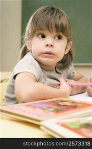 Close-up of a girl sitting at a desk and holding a colored pencil