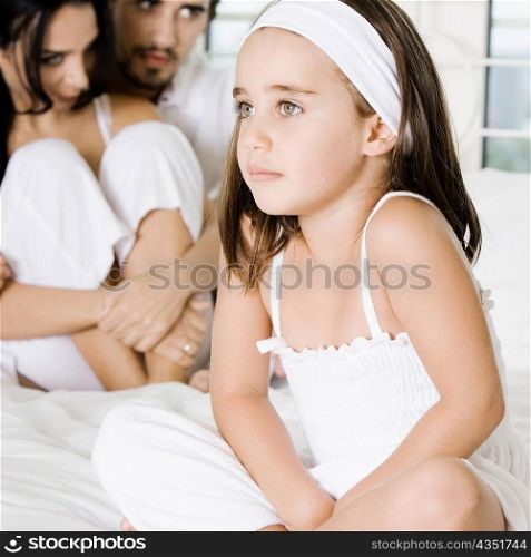 Close-up of a girl sitting on the bed with her parents behind her